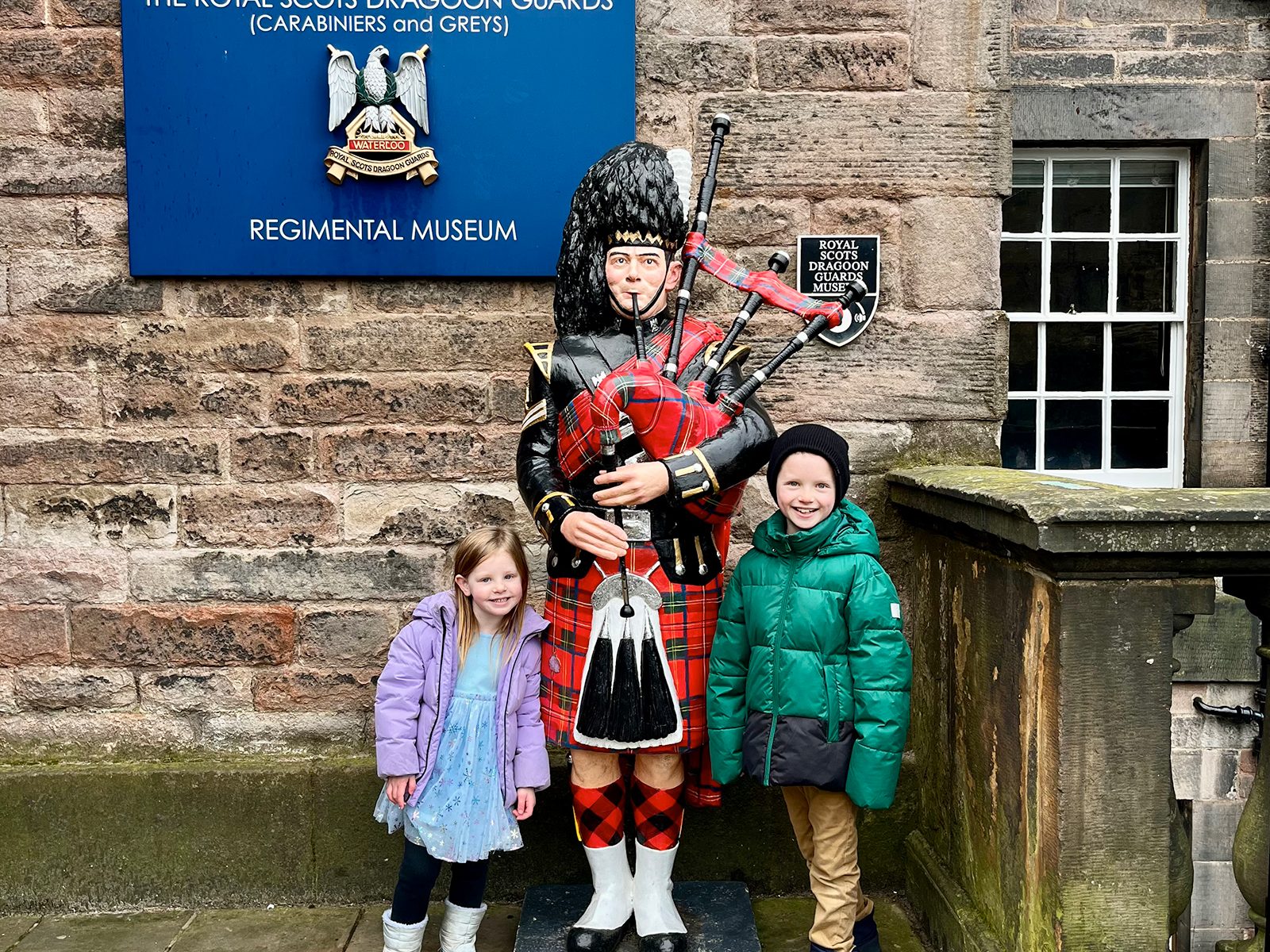 Calvin and Amelia posing with a bagpiper at Edinburgh Castle