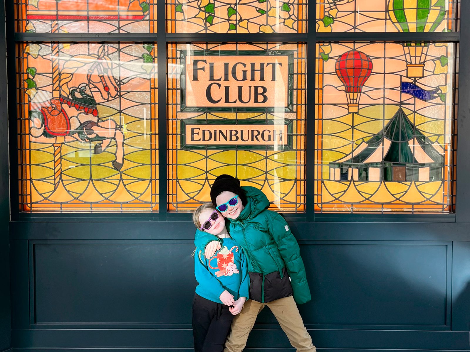 Calvin and Amelia hugging in front of the Flight Club Edinburgh stained glass window