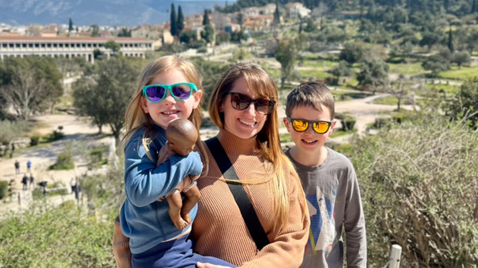 Carol holding Millie with Calvin beside them, the Acropolis on the hill behind